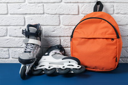 Pair of roller skates and backpack on blue table near white brick wallの写真素材