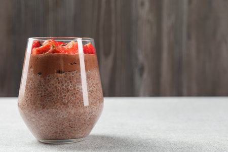 Delicious chocolate pudding with chia seeds and strawberries in glass on light gray table, closeup. Space for textの写真素材
