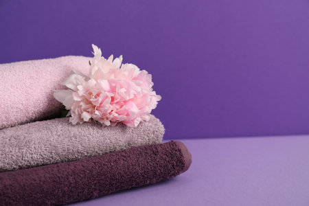 Stack of soft towels and peony flower on purple background, closeup. Space for textの写真素材