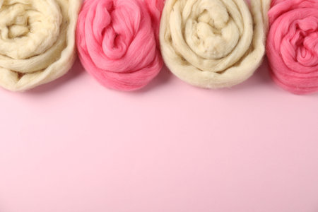 Colorful felting wool on pink background, flat lay. Space for text