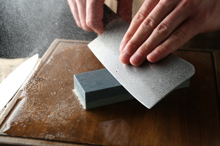 Man sharpening knife with sharpener on wooden table, closeupの写真素材