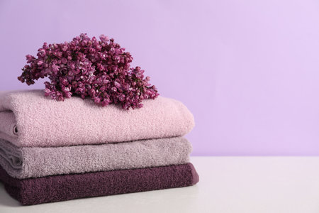 Soft towels and lilac flowers on white table against violet background, closeup. Space for textの写真素材