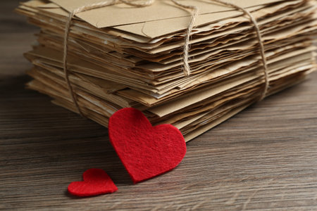 Stack of love letters and paper hearts on wooden table, closeup