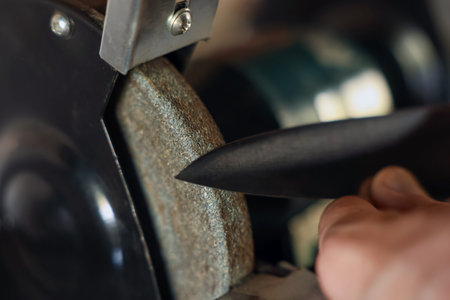 Man sharpening knife with bench grinder indoors, closeup