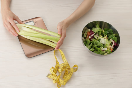 Woman weighing celery on kitchen scale at white wooden table, top viewの写真素材