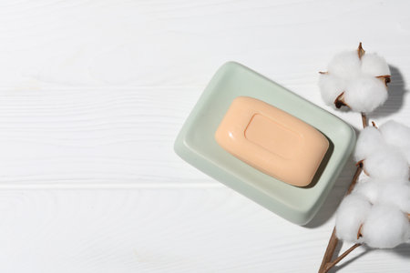Soap bar and cotton flowers on white wooden table, flat lay. Space for textの写真素材