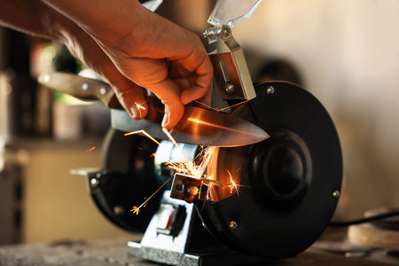 Man sharpening knife with bench grinder indoors, closeupの写真素材