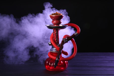 Hookah on wooden table with smoke in color lights against black background