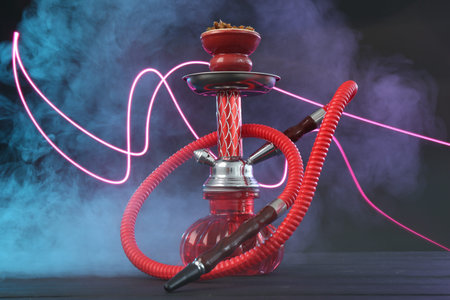Hookah on wooden table with smoke in color lights against black background
