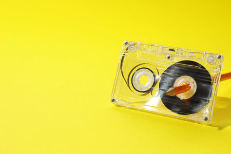 Rewinding audio cassette with pencil on yellow background, closeup. Space for textの写真素材
