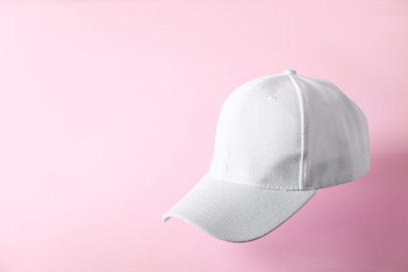 White baseball hat in air on pink background, space for text