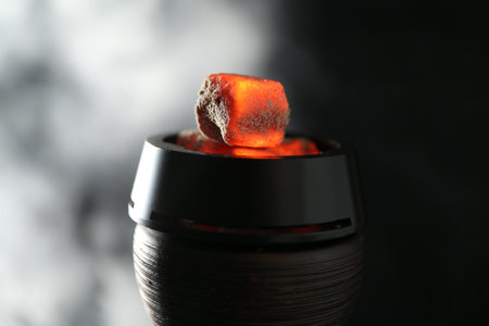 Smoldering charcoal cubes in hookah holder and smoke on dark background, closeup