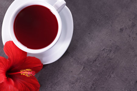 Tasty hibiscus tea in cup and beautiful flower on gray textured table, flat lay. Space for textの写真素材