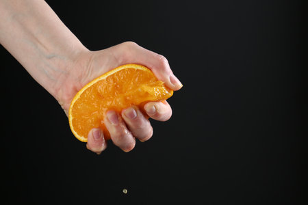 Woman squeezing orange on black background, closeup. Space for textの写真素材