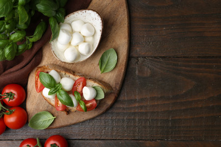 Tasty sandwich with mozzarella cheese, tomatoes and basil on wooden table, flat lay. Space for text