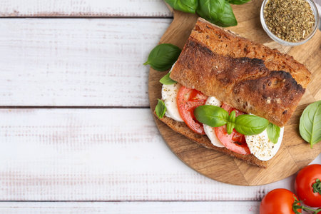 Tasty sandwich with mozzarella cheese, tomatoes and basil on white wooden table, flat lay. Space for textの写真素材