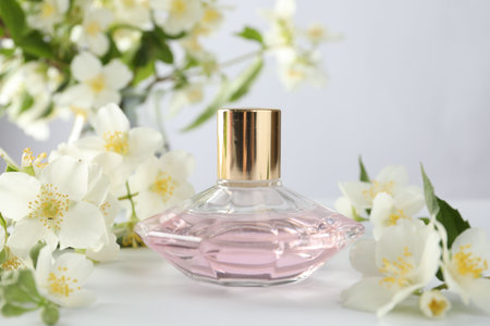 Bottle of perfume and jasmine flowers on white table, closeup