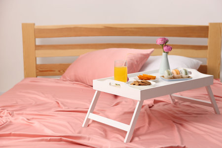 Tray with delicious breakfast and flowers on bed indoors. Space for text