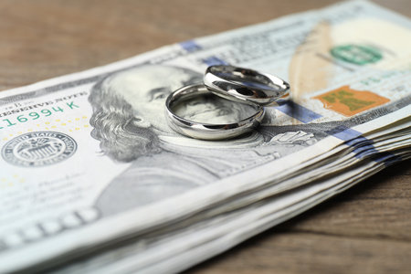 Silver wedding rings and dollar banknotes on wooden table, closeupの写真素材