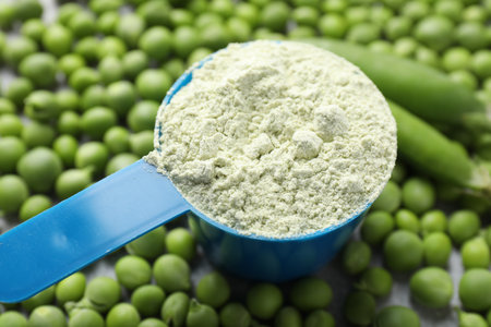 Protein powder in measuring spoon on fresh green peas, closeupの写真素材