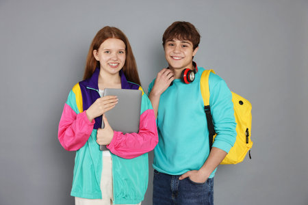 Teenagers with backpack and laptop on gray background