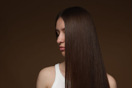 Teenage girl with healthy long hair on brown background