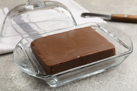 Block of tasty chocolate butter in glass keeper on gray textured table, closeupの写真素材
