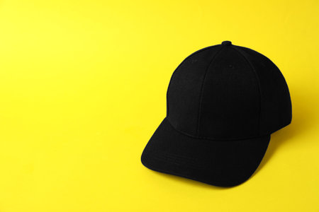 Black baseball hat on yellow background, space for textの写真素材