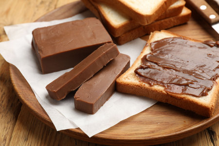 Pieces of tasty chocolate butter and slices of bread on wooden table, closeup