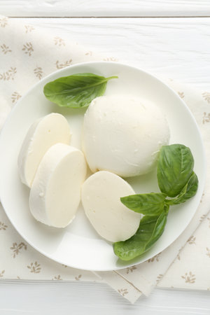 Pieces of delicious mozzarella cheese and basil on white wooden table, top viewの写真素材