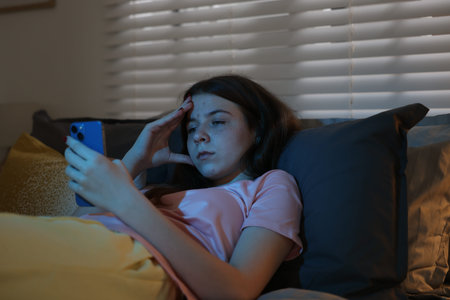 Upset teenage girl with smartphone on bed at night