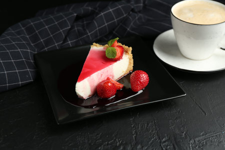 Piece of tasty cheesecake with strawberries, sauce, mint and coffee on black table, closeup