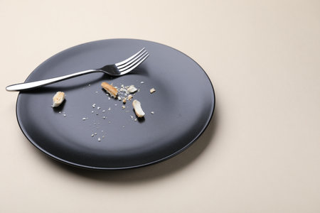 Dirty plate with bread crumbs and fork on beige background, closeup. Space for textの写真素材