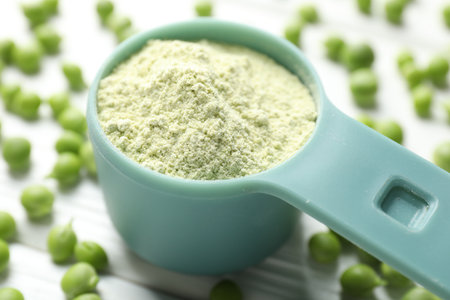 Protein powder in measuring spoon and green peas on white wooden table, closeupの写真素材