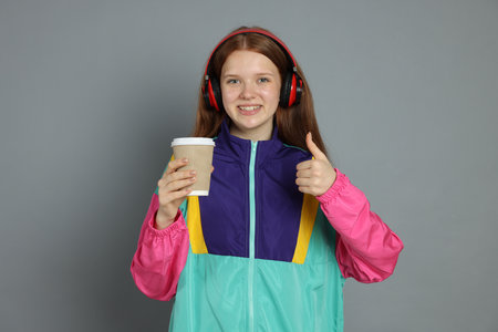 Teenage girl with drink showing thumbs up on grey backgroundの写真素材