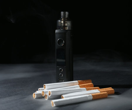 Electronic smoking device and cigarettes on dark table against black background, closeupの写真素材