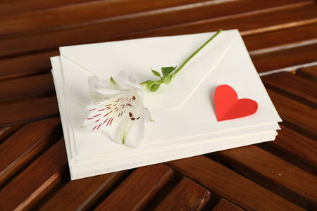 Stack of love letters, red heart and flower on wooden table, above view