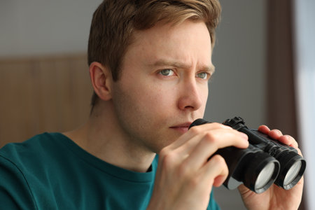 Paranoia. Worried man with binoculars at homeの写真素材