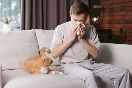 Man suffering from allergy with his cat on sofa at homeの写真素材