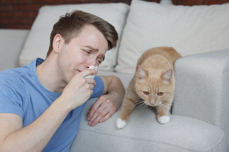 Man suffering from allergy with his cat at homeの写真素材