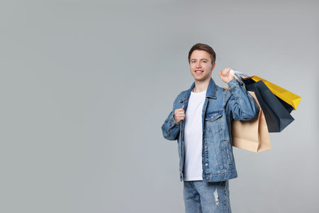 Cheerful man with shopping bags on light gray background. Space for text