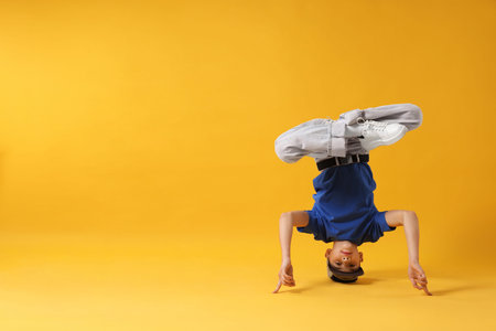 Boy in stylish clothes dancing on orange background, space for text
