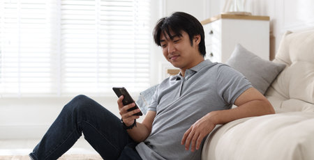 Handsome Asian man with smartphone at home