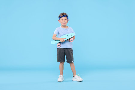 Little boy with penny board on light blue background