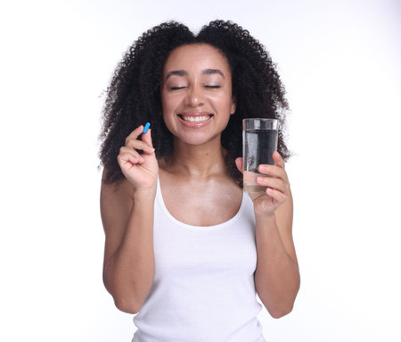 Beautiful Brazilian woman with glass of water and collagen pill on white backgroundの写真素材