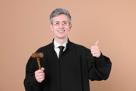 Smiling judge with mallet showing thumbs up on beige backgroundの写真素材