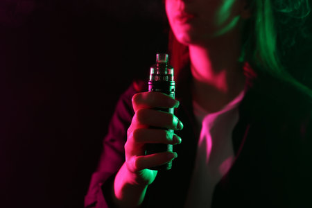 Woman using electronic smoking device in neon lights on black background, closeup. Space for text