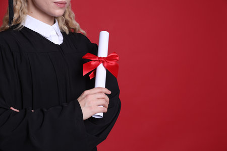 Student with diploma after graduation on red background, closeup. Space for textの写真素材
