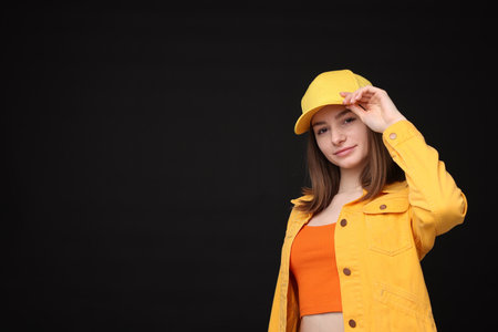 Young woman wearing stylish yellow baseball hat on black background, space for textの写真素材