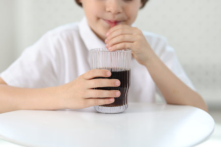 Little boy drinking refreshing soda at table indoors, closeup
